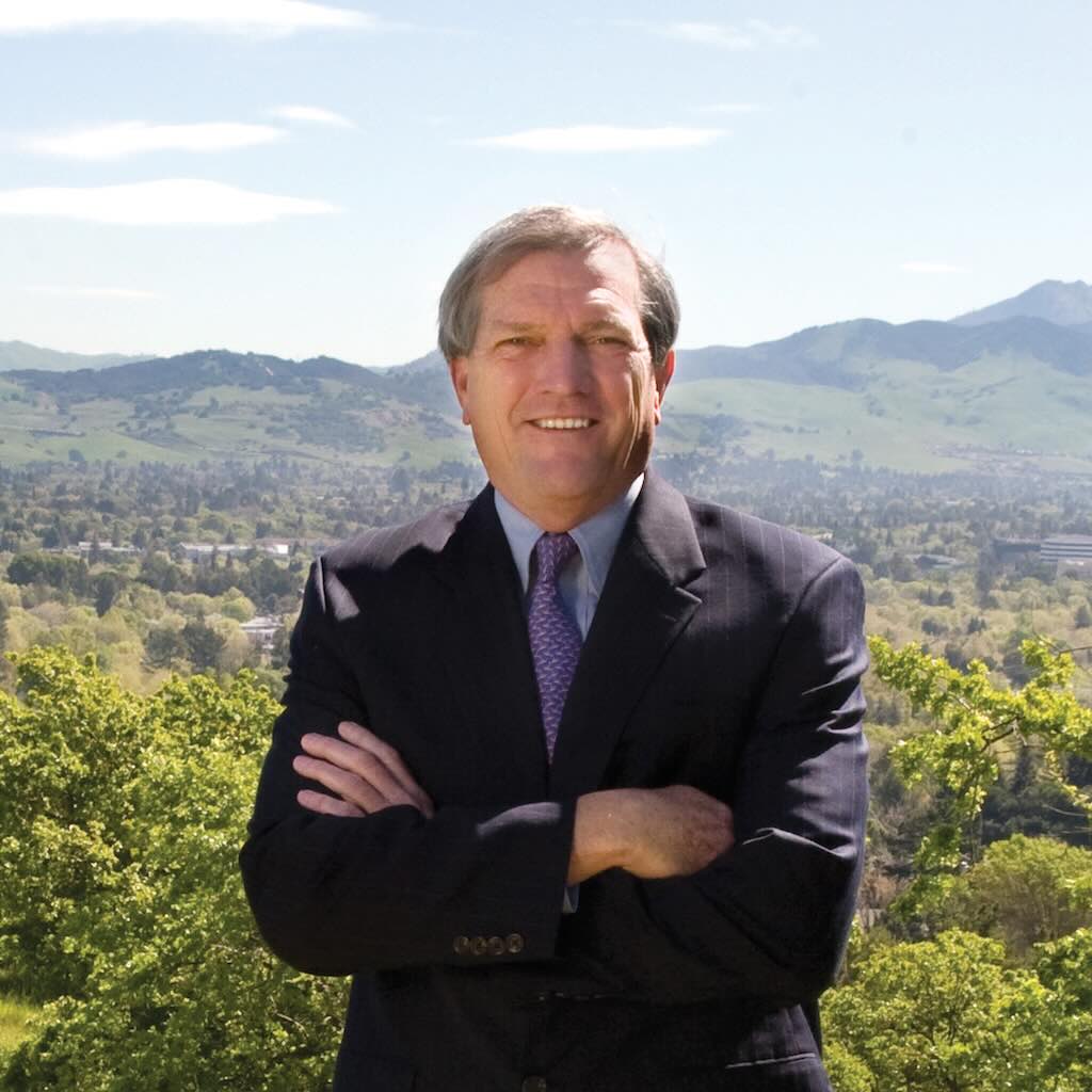 US House District 10 candidate Mark DeSaulnier Man in a suit smiles at the camera in front on a backdrop of green hills