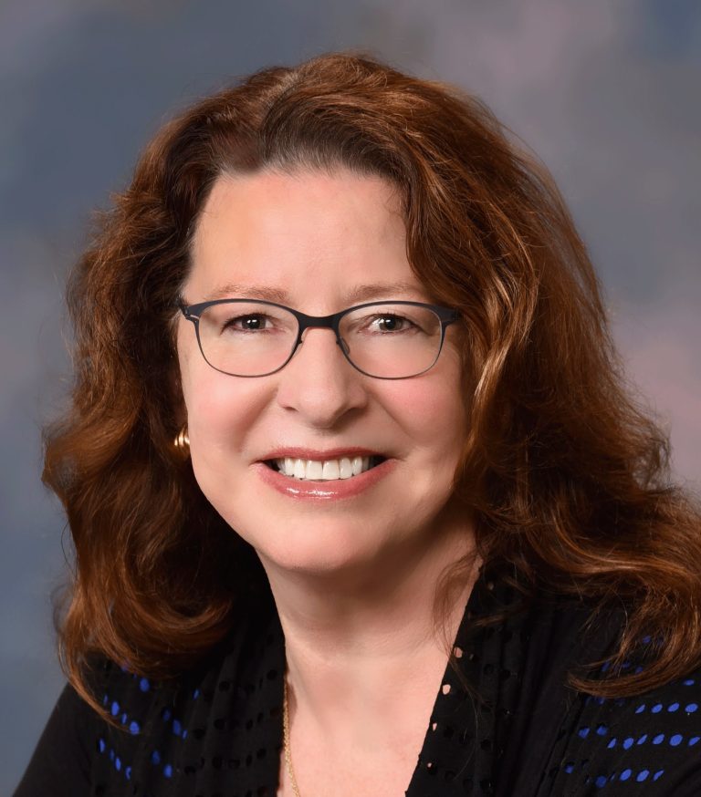 Ann Schneider for Millbrae City Council District 3. Woman with auburn hair and glasses, smiling. Ann Schneider, used with permission.