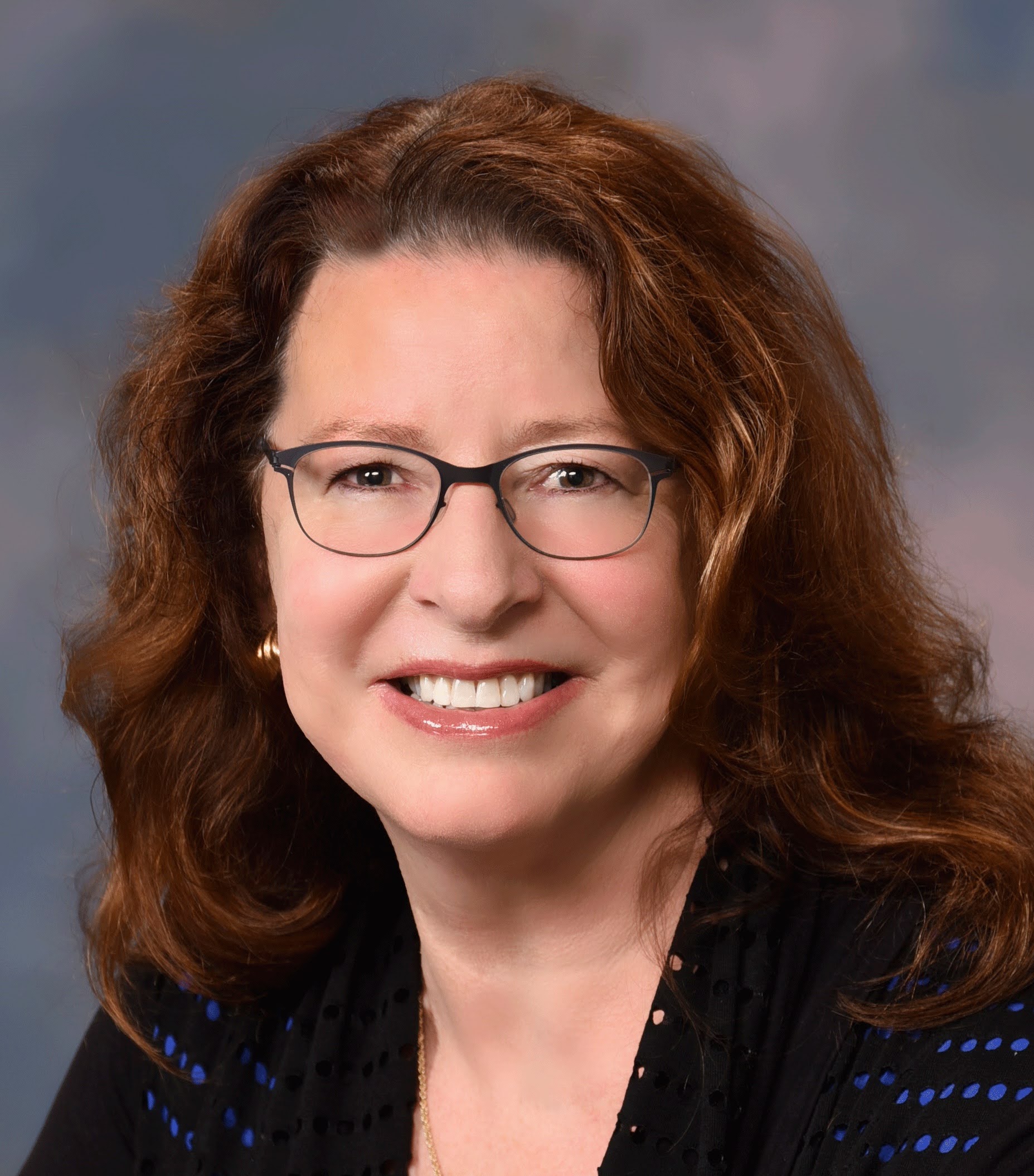 Ann Schneider for Millbrae City Council District 3. Woman with auburn hair and glasses, smiling. Ann Schneider, used with permission.