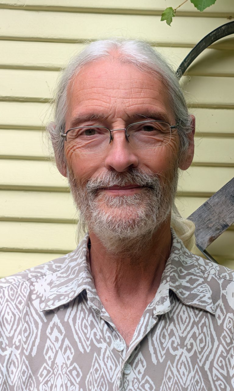 Bruce Ackerman for Fairfax Town Clerk. Man with rimless glasses, looking peaceful in front of a house. Photo credit: Bruce Ackerman, used with permission.