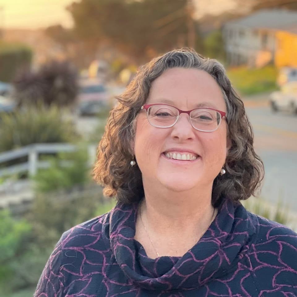 Christine Boles for Pacifica City Council District 2 Woman with a big smile, horn-rimmed glasses and a blue and purple cowl-neck sweater. Photo credit: Christine Boles, used with permission.