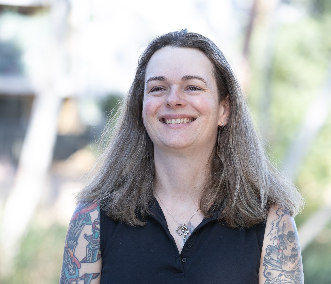 Robyn Kuslits for Concord City Council, District 3. Robyn stands, with shoulder-length hair and tattooed arms, smiling brightly. Photo credit: Robyn Kuslits, used with permission
