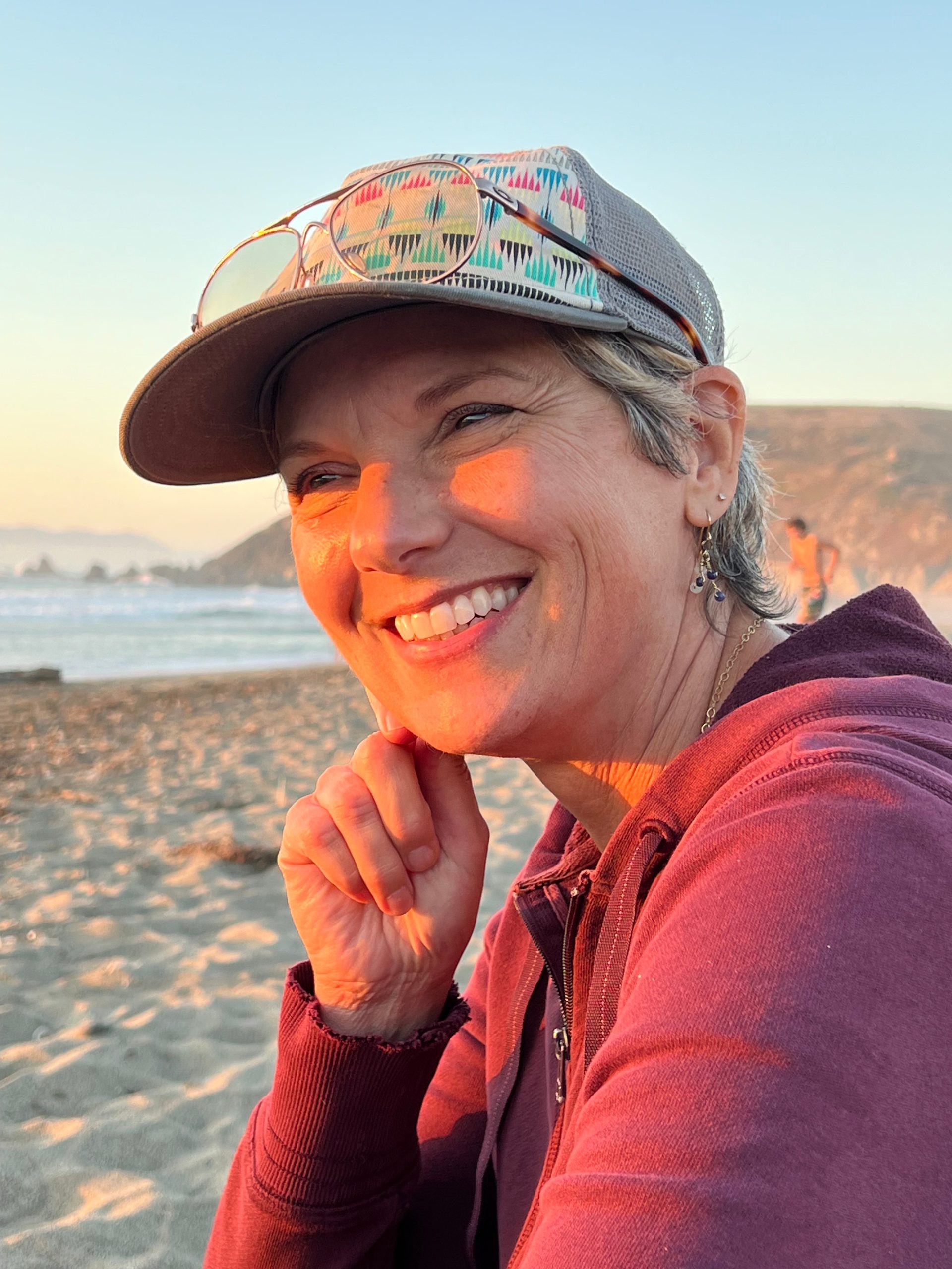 Margo Meiman for Pacifica District 5. Woman sitting on the beach, smiling, looking at the coastline. Photo credit: Linda Slack, used with permission