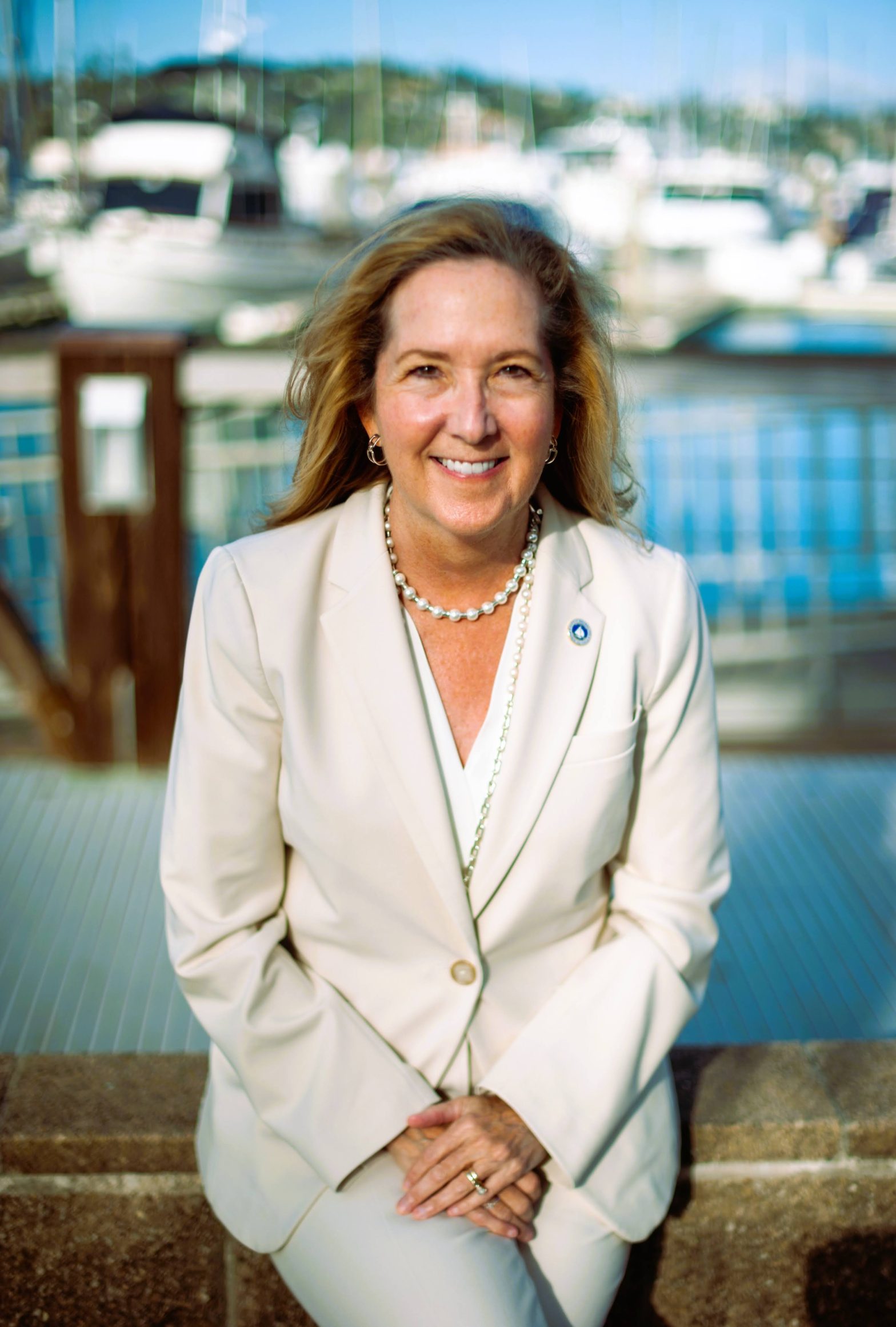 Jill Hoffman for Sausalito City Council. Woman in an off-white colored suit, smiling with the Sausalito harbor behind her. Photo credit: Jill Hoffman, used with permission.