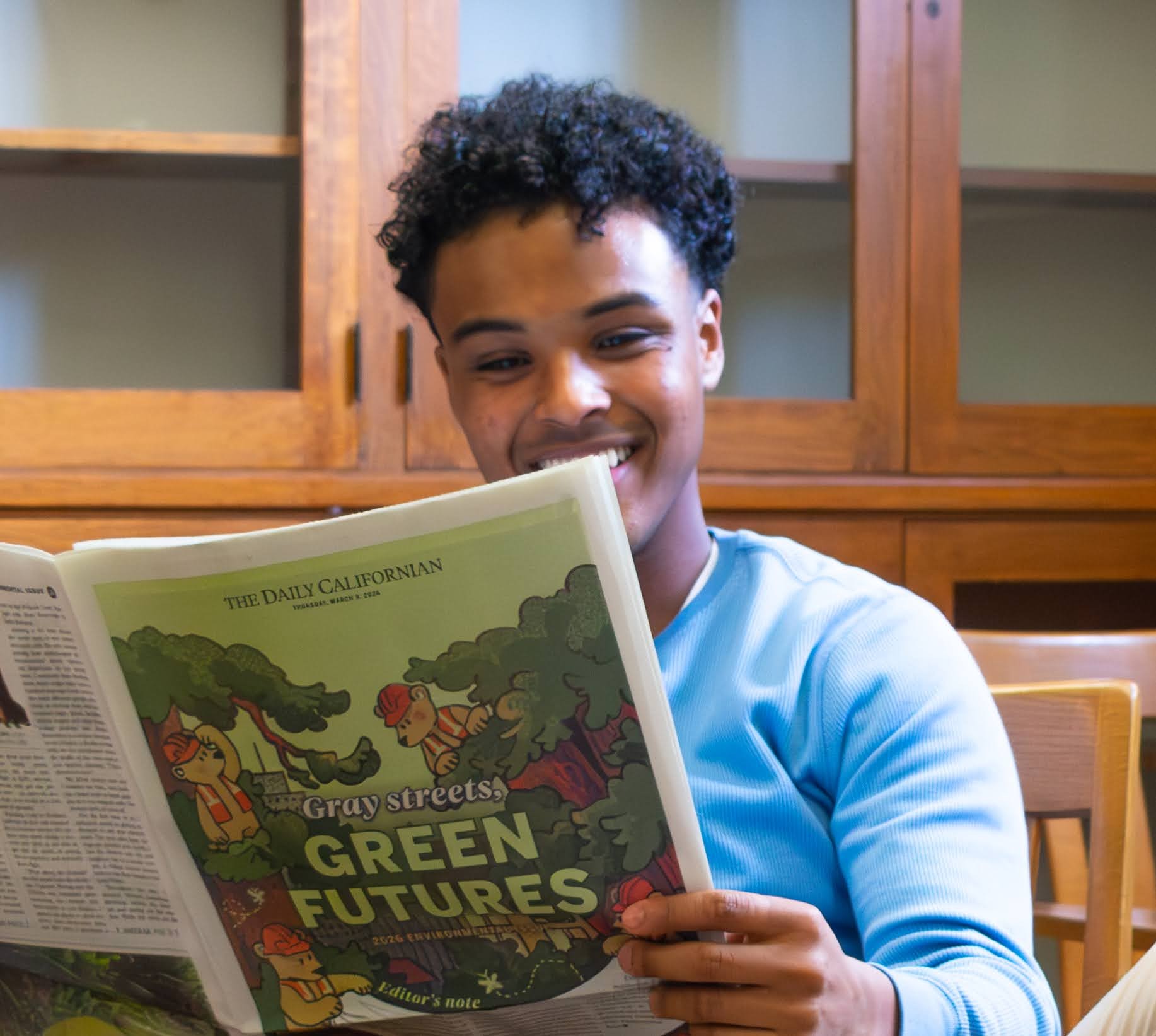 Syrak Micael for Berkeley City Council district 7. Young man in a light blue sweatshirt, reading the Daily Californian "Green Futures" feature. Photo credit: Marissa Oaks English, used with permission.
